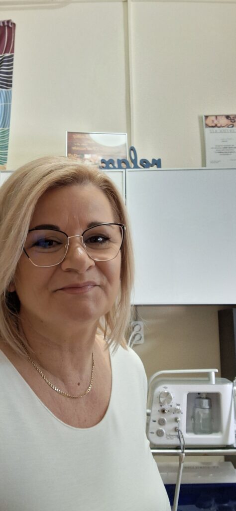 Mosolygó masszőr és pedikűrös egy világos, tiszta kezelőhelyiségben, háttérben pedikűr- és kozmetikai eszközökkel.